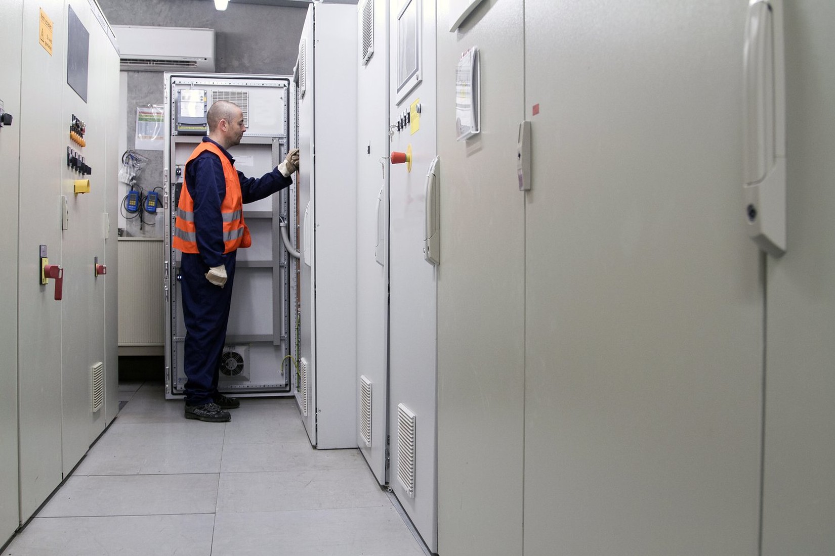 Elektryk w kamizelce odblaskowej przy szafach rozdzielczych w pomieszczeniu technicznym Elektryk w kamizelce odblaskowej przy szafach rozdzielczych w pomieszczeniu technicznym